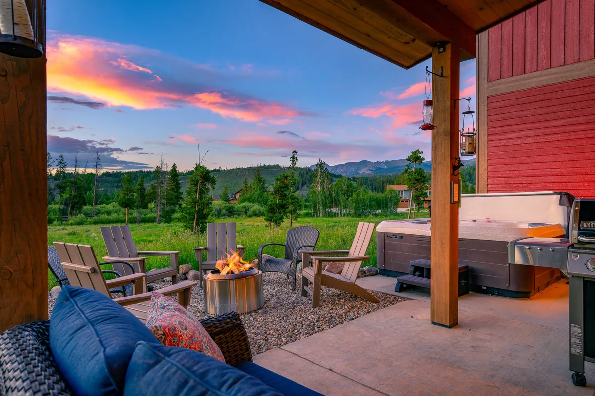 This exterior scene features a cozy fire pit and a hot tub set on a patio, with comfortable outdoor seating and a stunning mountain view in the background. The setup encourages relaxation and social connection, offering a perfect spot to unwind after a day of adventure.