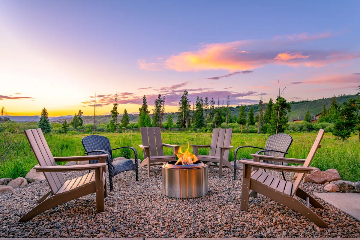A cozy outdoor fire pit area, surrounded by Adirondack chairs and set against a stunning sunset sky. The space encourages communal gatherings, story-telling, and stargazing, spotlighting outdoor relaxation and leisure.