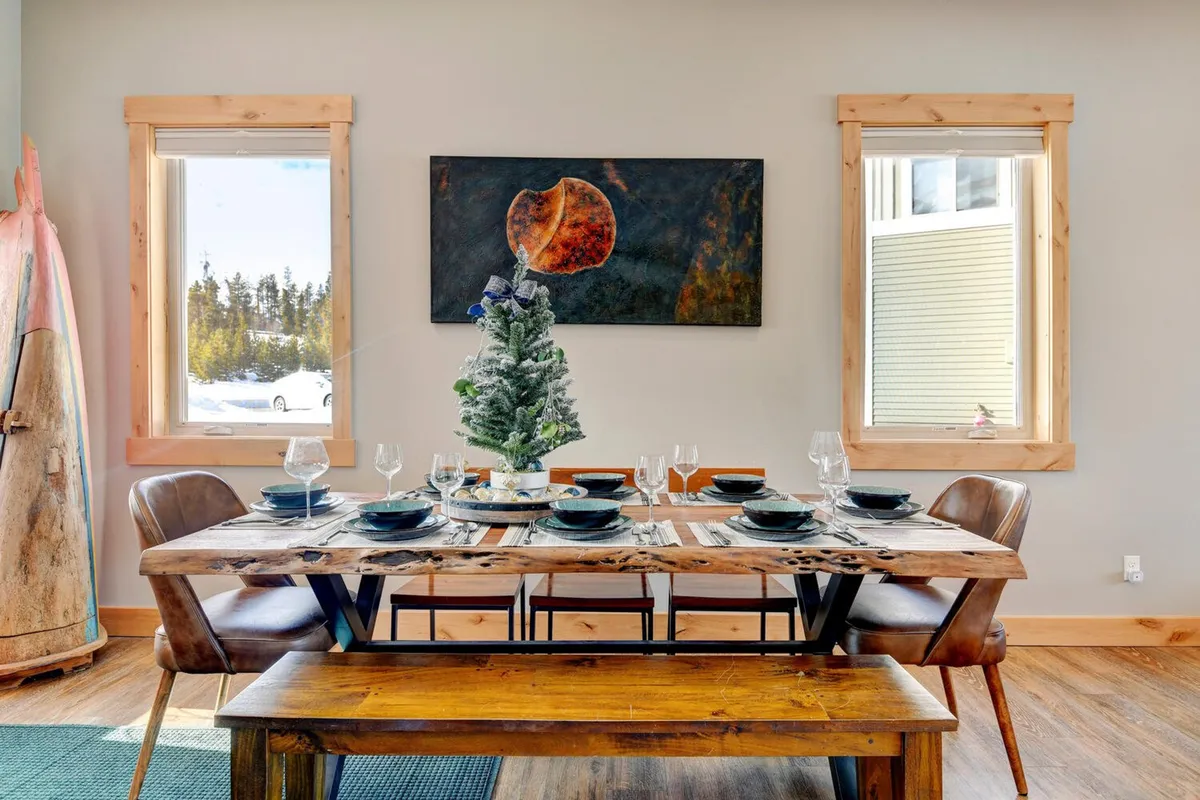 A warm and welcoming dining area featuring a large wooden dining table that seats eight, a decorative painting on the wall, and windows that bring in natural light. The space is set for festive meals and group gatherings.