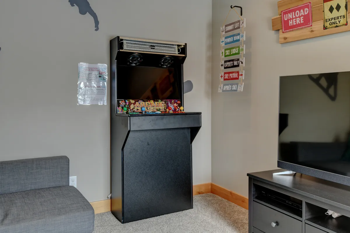 A fun and casual lounge area with a retro arcade game machine, a television, and a sofa, perfect for entertaining groups. The space is designed for both play and relaxation, inviting friendly competition and shared experiences.