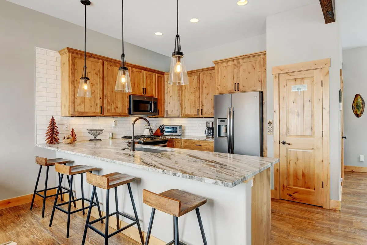 A cozy, modern kitchen with custom granite countertops, wooden cabinets, stylish pendant lights, and bar stools at the island. The space is clearly designed for both cooking and casual gatherings, providing ample prep area for multiple cooks and a welcoming atmosphere.